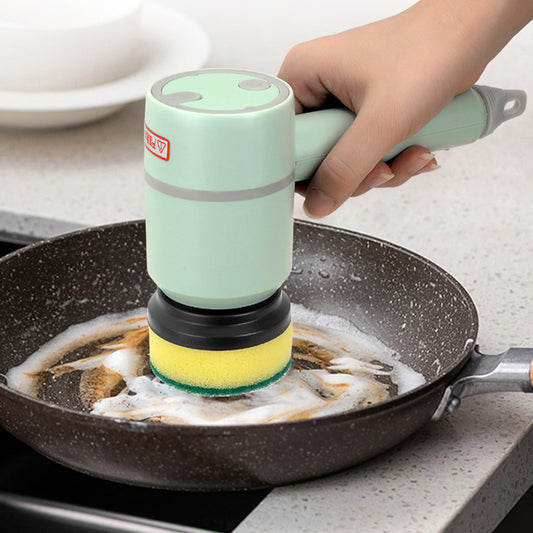 Hand using a green handheld scrubber to clean a frying pan on a kitchen counter.
